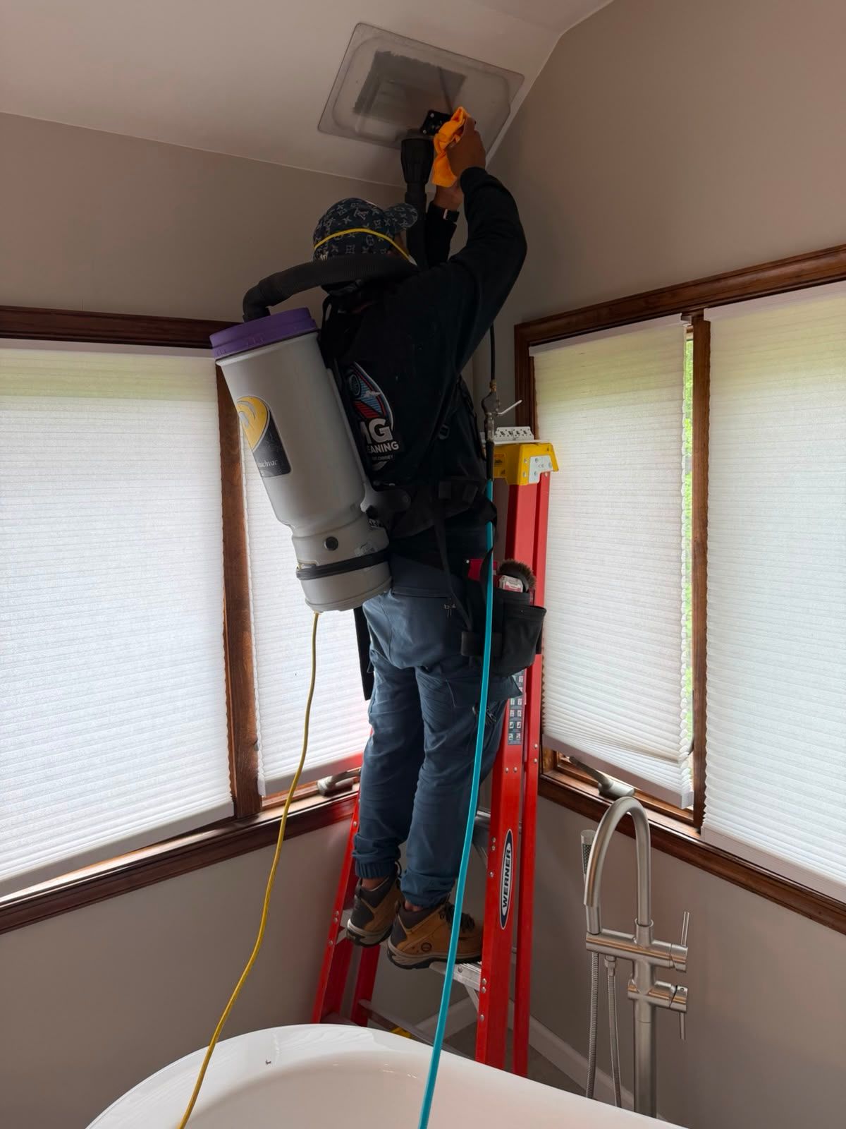 AMG technician with a backpack HEPA vacuum cleaning a ceiling supply register