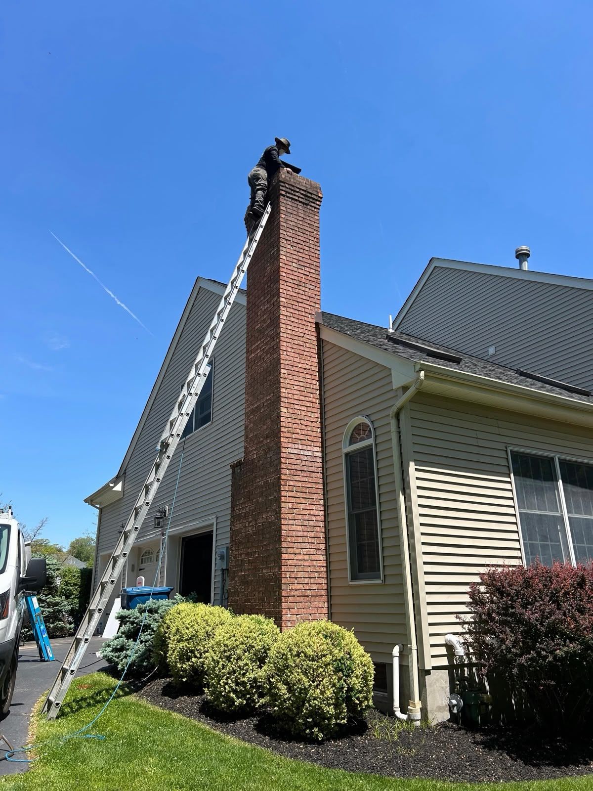 AMG technician at the top of a tall red brick chimney on an extension ladder