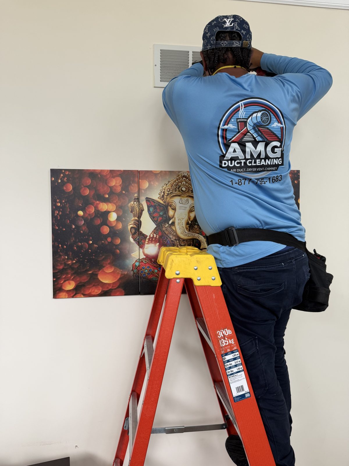 An AMG technician on a ladder cleaning a ceiling vent register