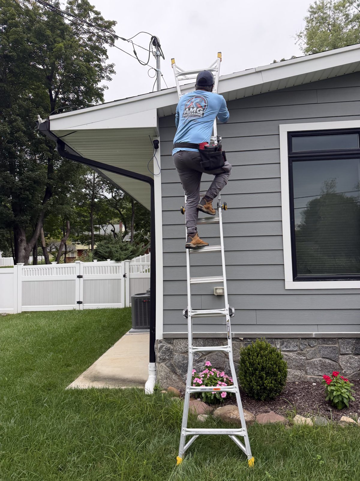 An AMG technician on an extension ladder at a house chimney