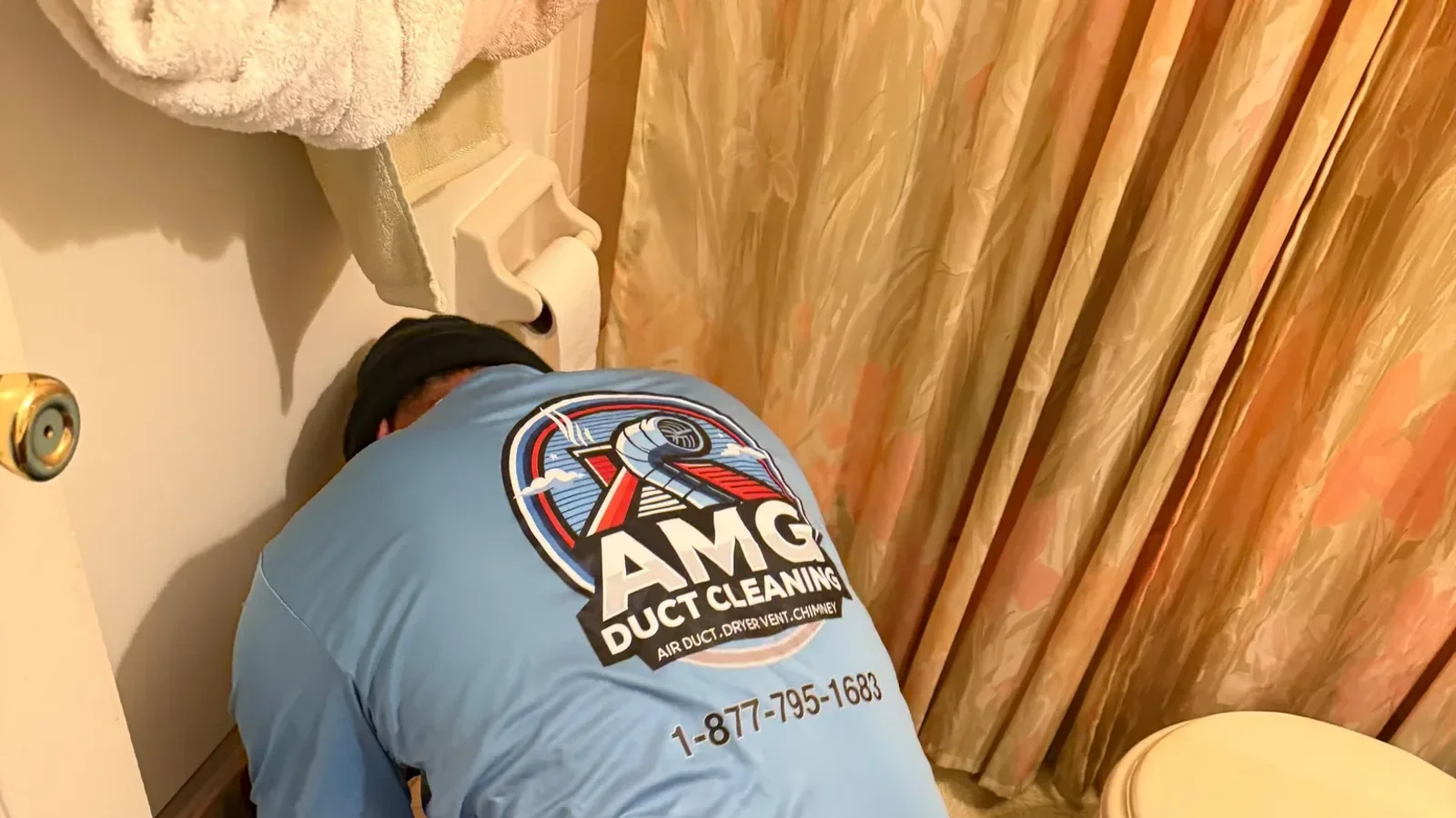A technician in a blue uniform crouching beside an open floor-level supply vent in a vintage-style Elizabeth NJ living r