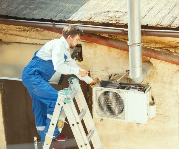 HVAC technician working on a capacitor part for condensing unit. Male worker or repairman in uniform repairing and adjusting conditioning system, diagnosting and looking for technical issues.